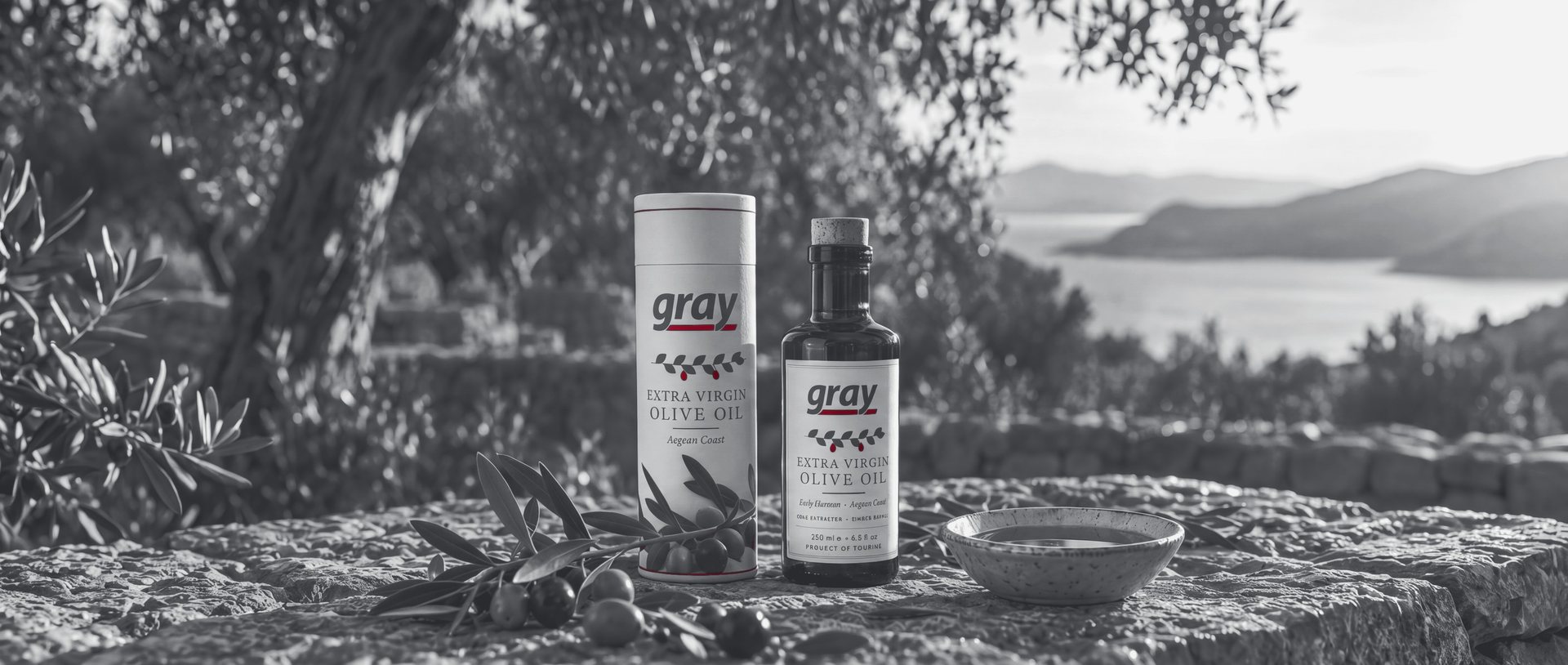 Gray cylinder tube and labelled olive oil bottle in an Aegean olive grove